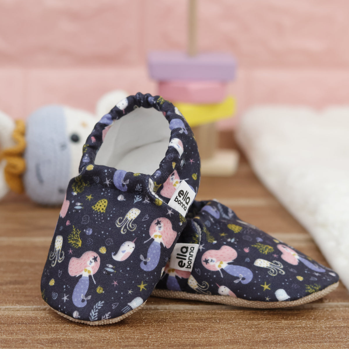 Navy slip-on baby moccasins with mermaids and sea-creature print arranged together to show the sides and uppers.
