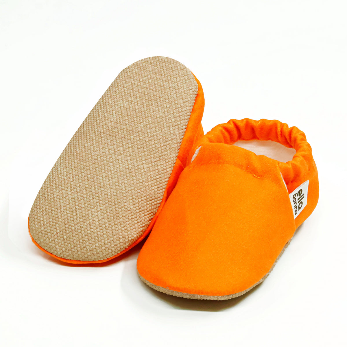Orange slip-on baby moccasins with cream lining and tan soles, with one sole facing the camera on a white background.