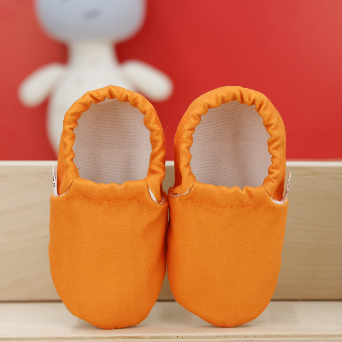 Pair of orange slip-on baby moccasins with cream lining and tan soles, showing the openings and uppers.