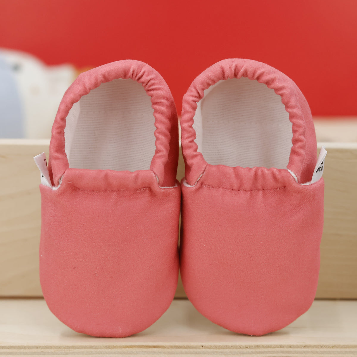 Pair of coral pink slip-on baby moccasins with cream lining and tan soles, showing the openings and uppers.