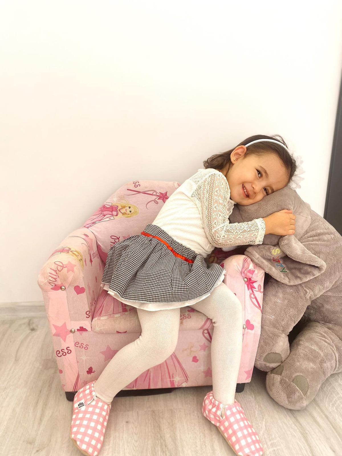 Child reclining in a small chair wearing pink gingham moccasins.