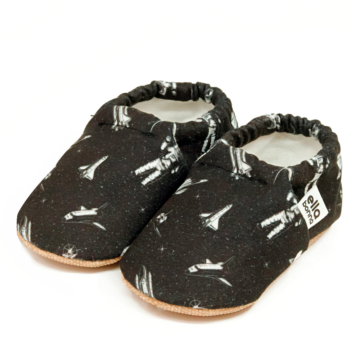 Pair of black slip-on baby moccasins with white astronaut and spacecraft print on a white background.