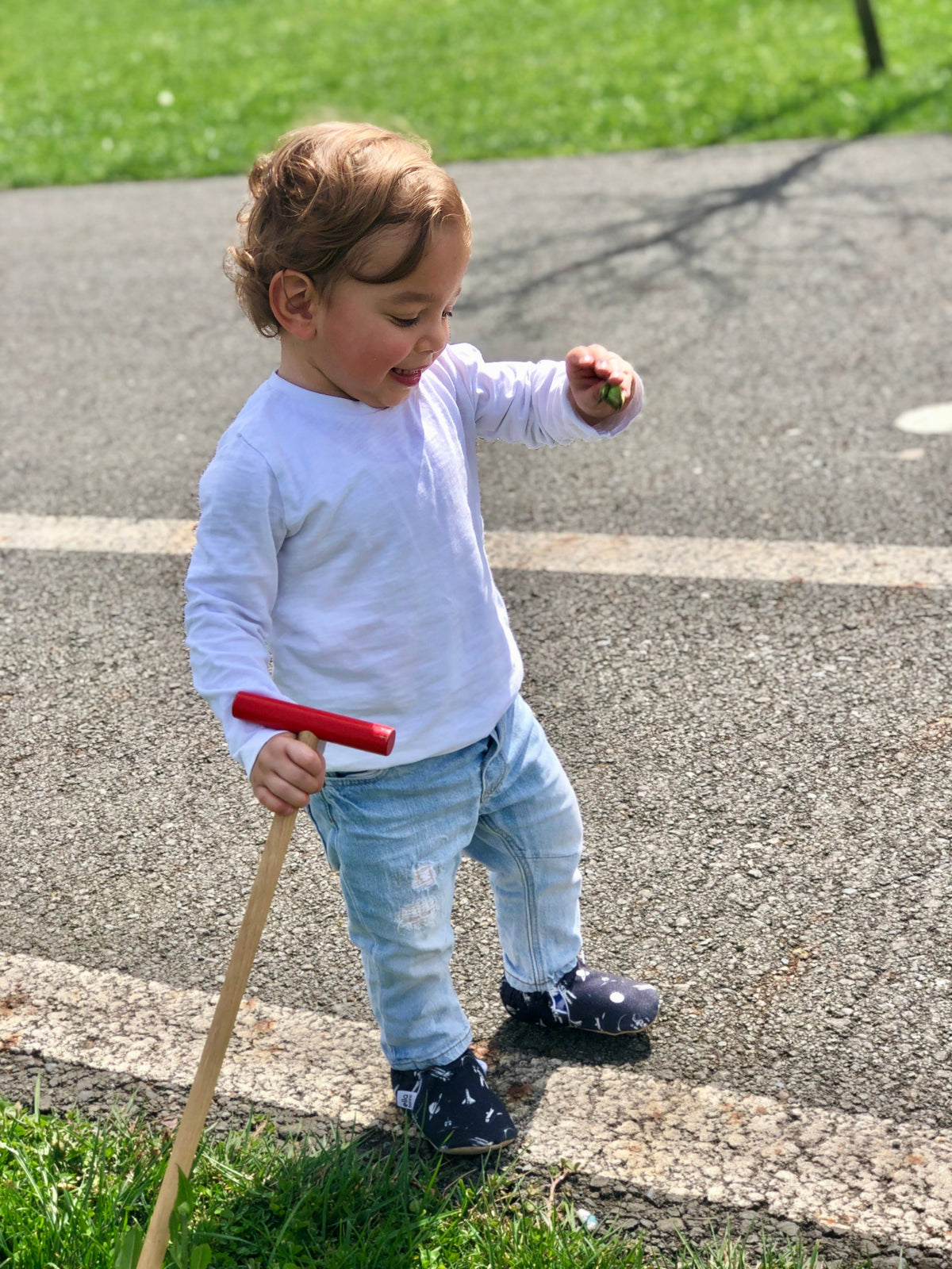 Child standing beside a push toy on pavement wearing dark moccasins.