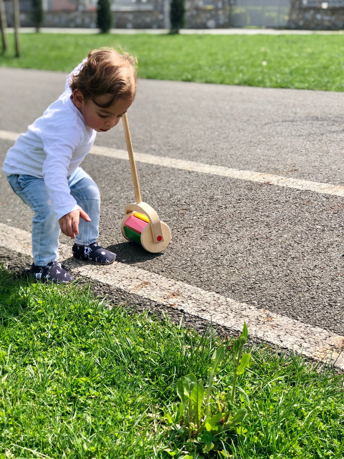 Child crouching beside a push toy outdoors wearing dark moccasins.