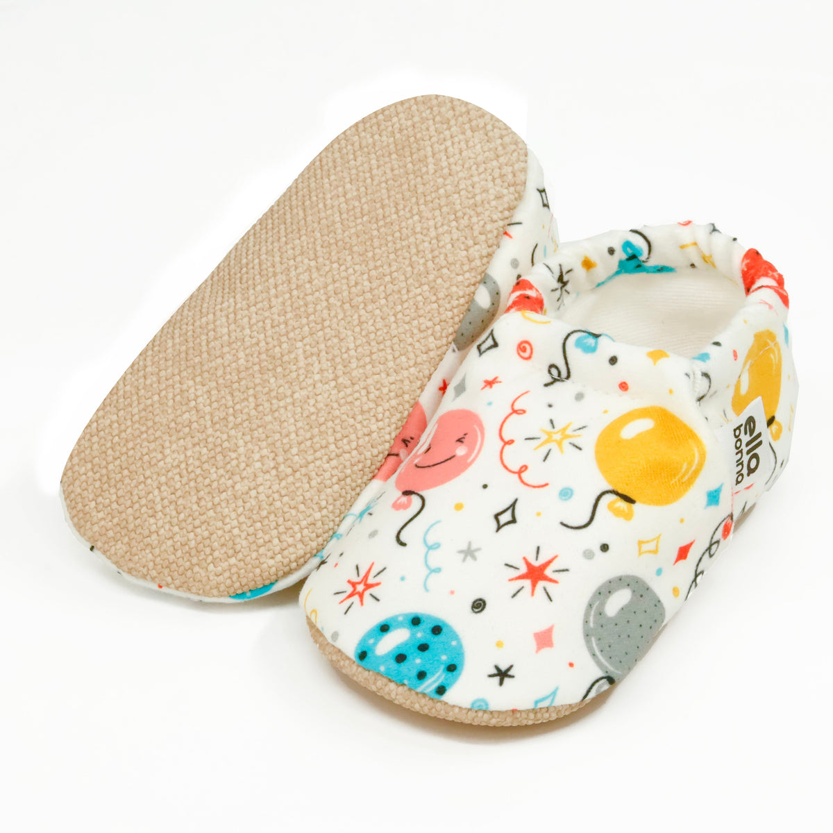 Cream slip-on baby moccasins with colorful balloon print, with one sole facing the camera on a white background.