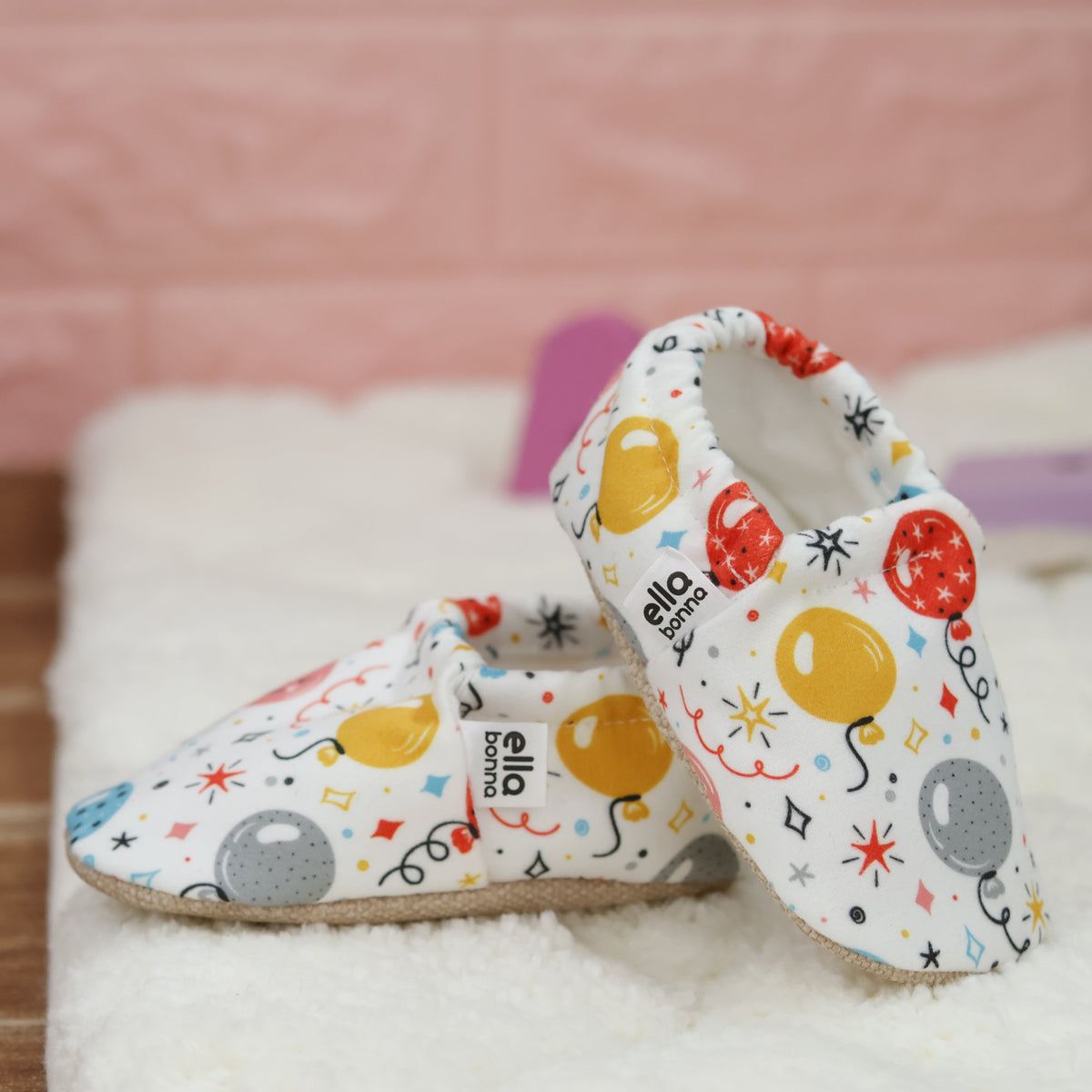 Cream slip-on baby moccasins with colorful balloon print arranged together to show the sides and uppers.