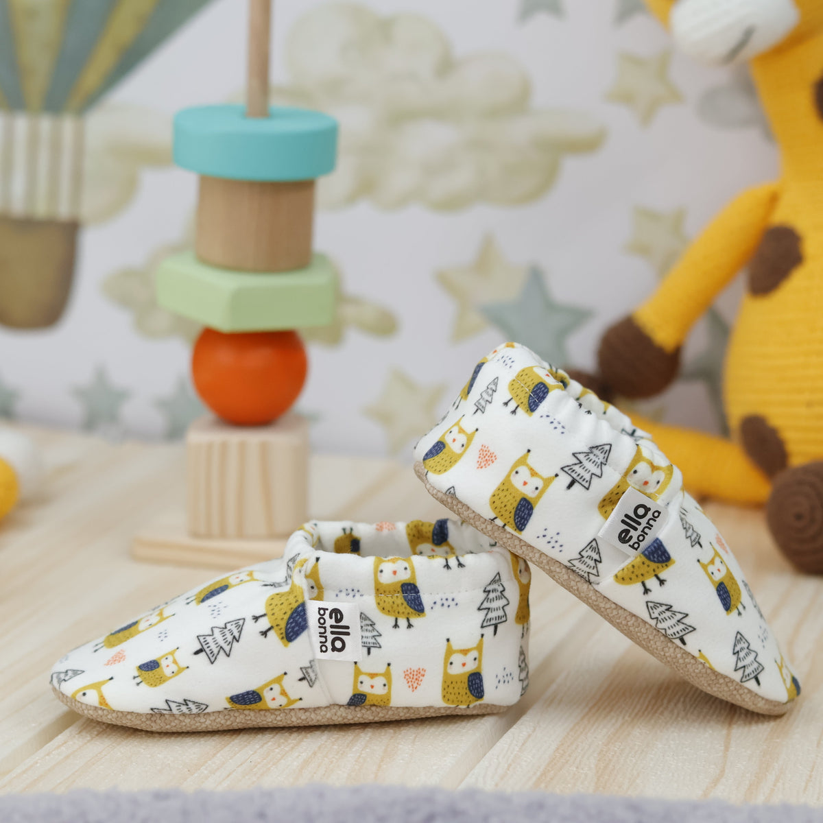 Cream slip-on baby moccasins with yellow owl and tree print arranged together to show the sides and uppers.