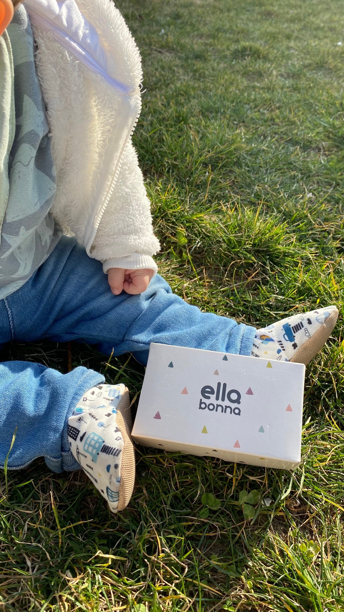 Close view of a seated child with city-print moccasins and an Ella Bonna card.