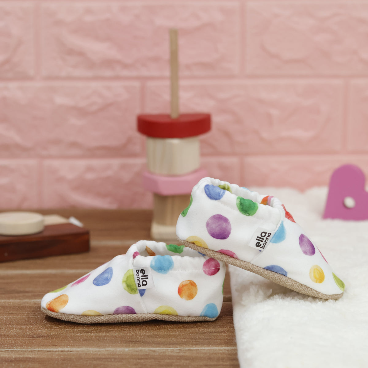 White slip-on baby moccasins with multicolored watercolor dot print arranged together to show the sides and uppers.