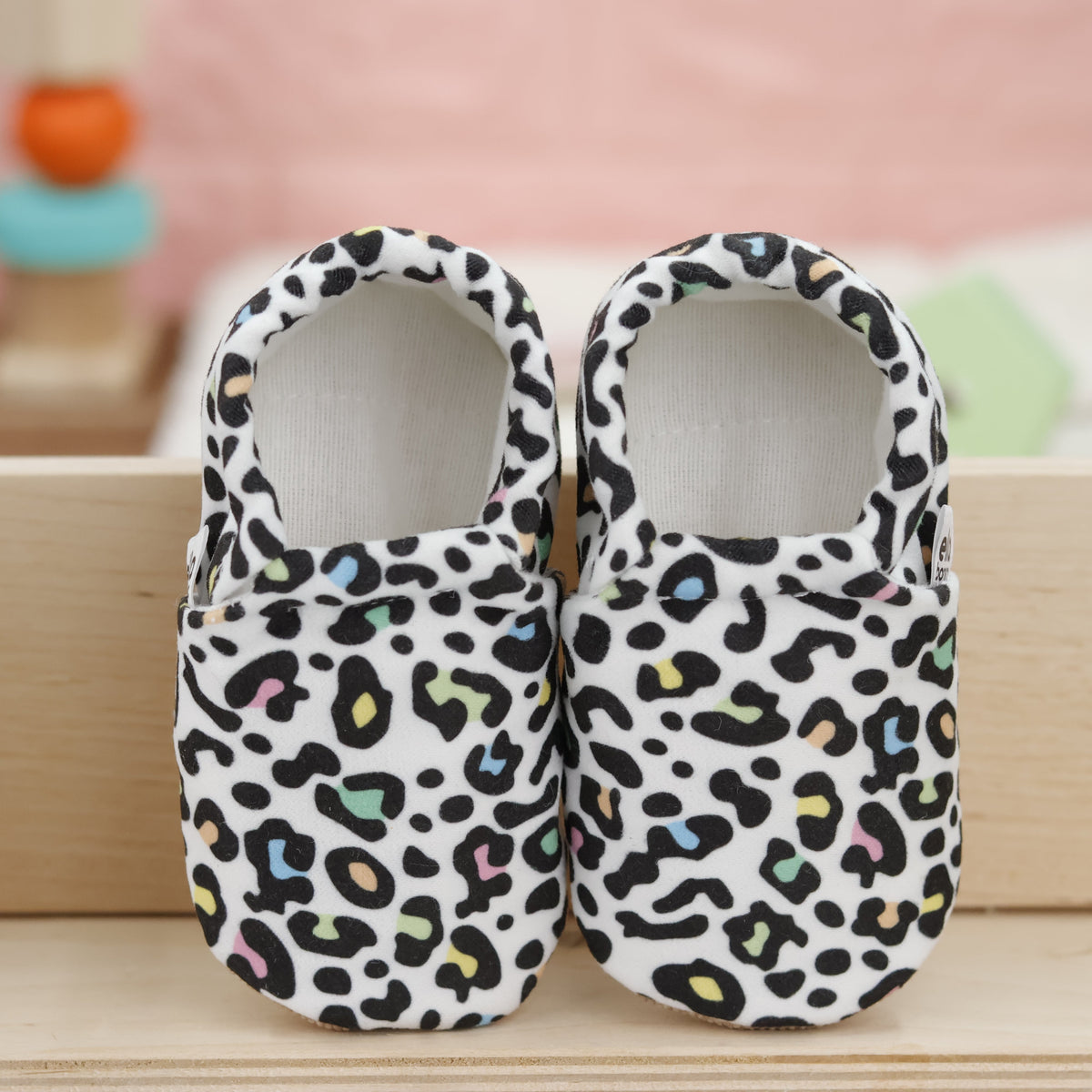 Pair of cream slip-on baby moccasins with multicolored leopard spots, showing the openings and uppers.
