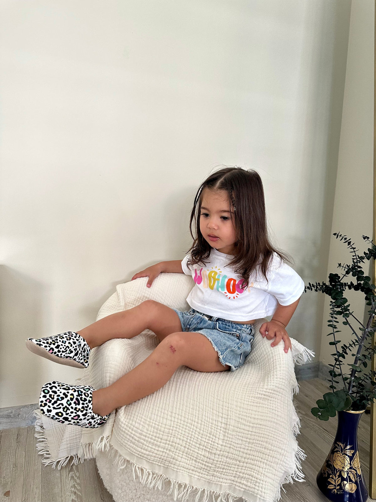 Child reclining on a chair wearing leopard-print moccasins.