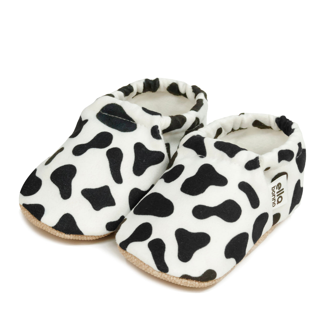 Pair of white slip-on baby moccasins with black cow spots on a white background.