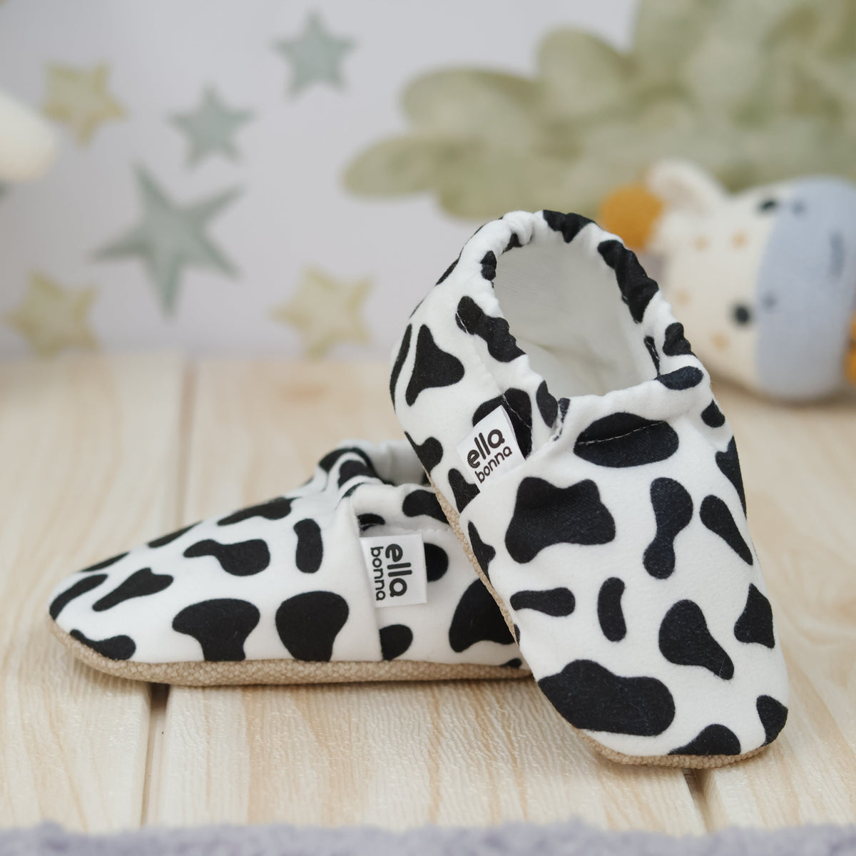 White slip-on baby moccasins with black cow spots arranged together to show the sides and uppers.