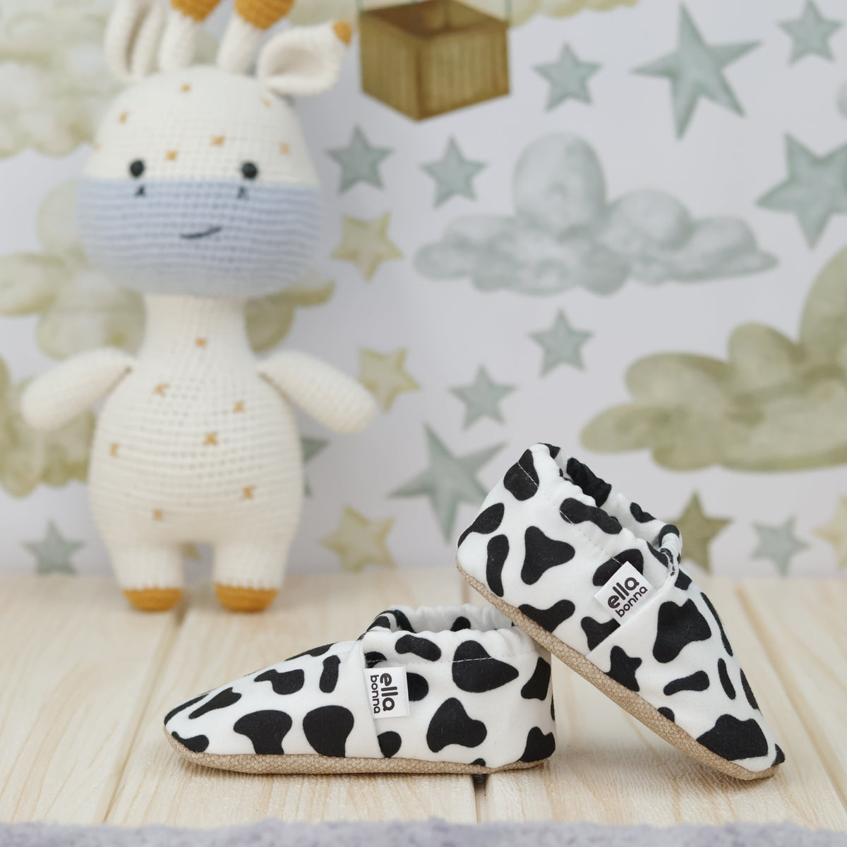 White slip-on baby moccasins with black cow spots arranged together to show the sides and uppers.