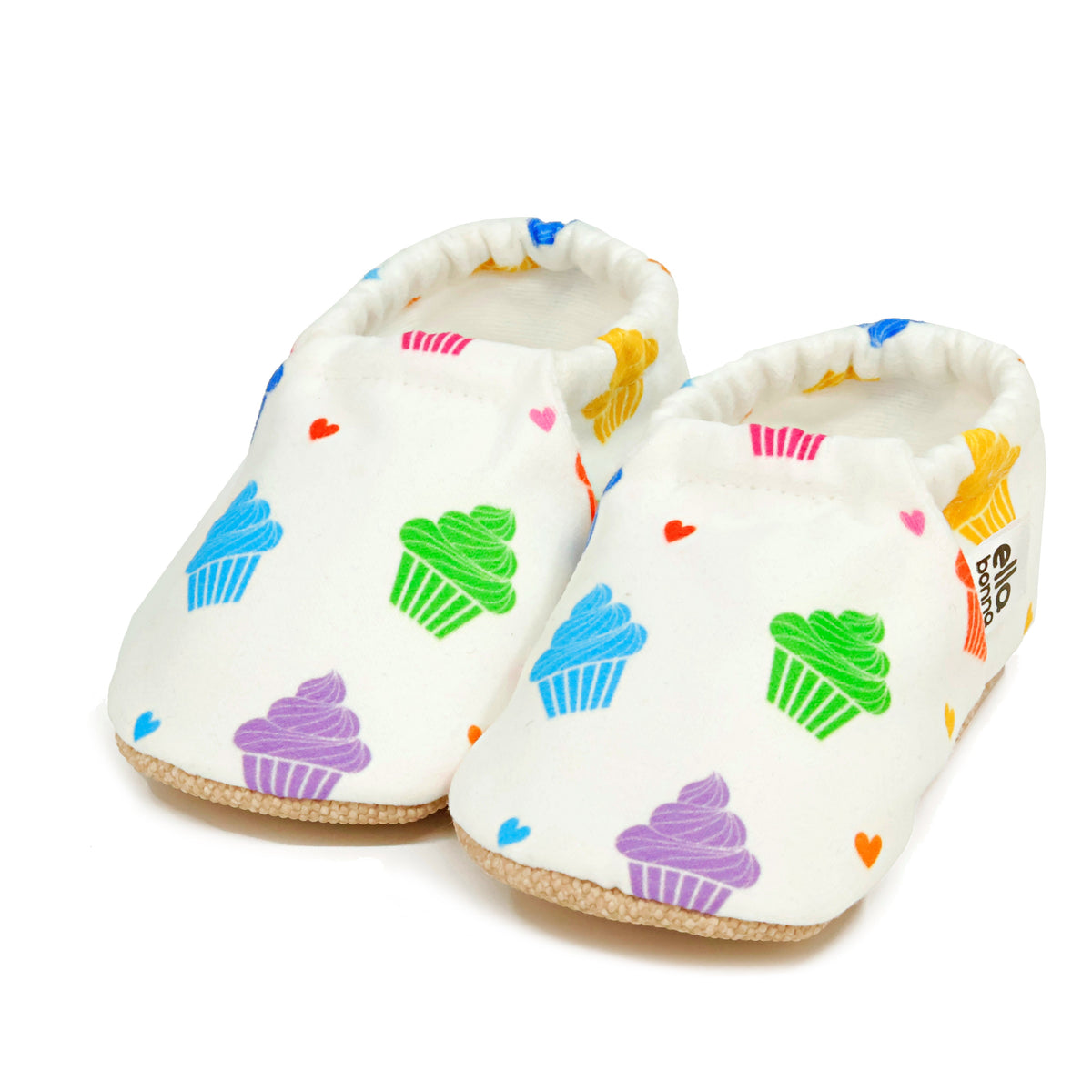 Pair of white slip-on baby moccasins with colorful cupcake print on a white background.