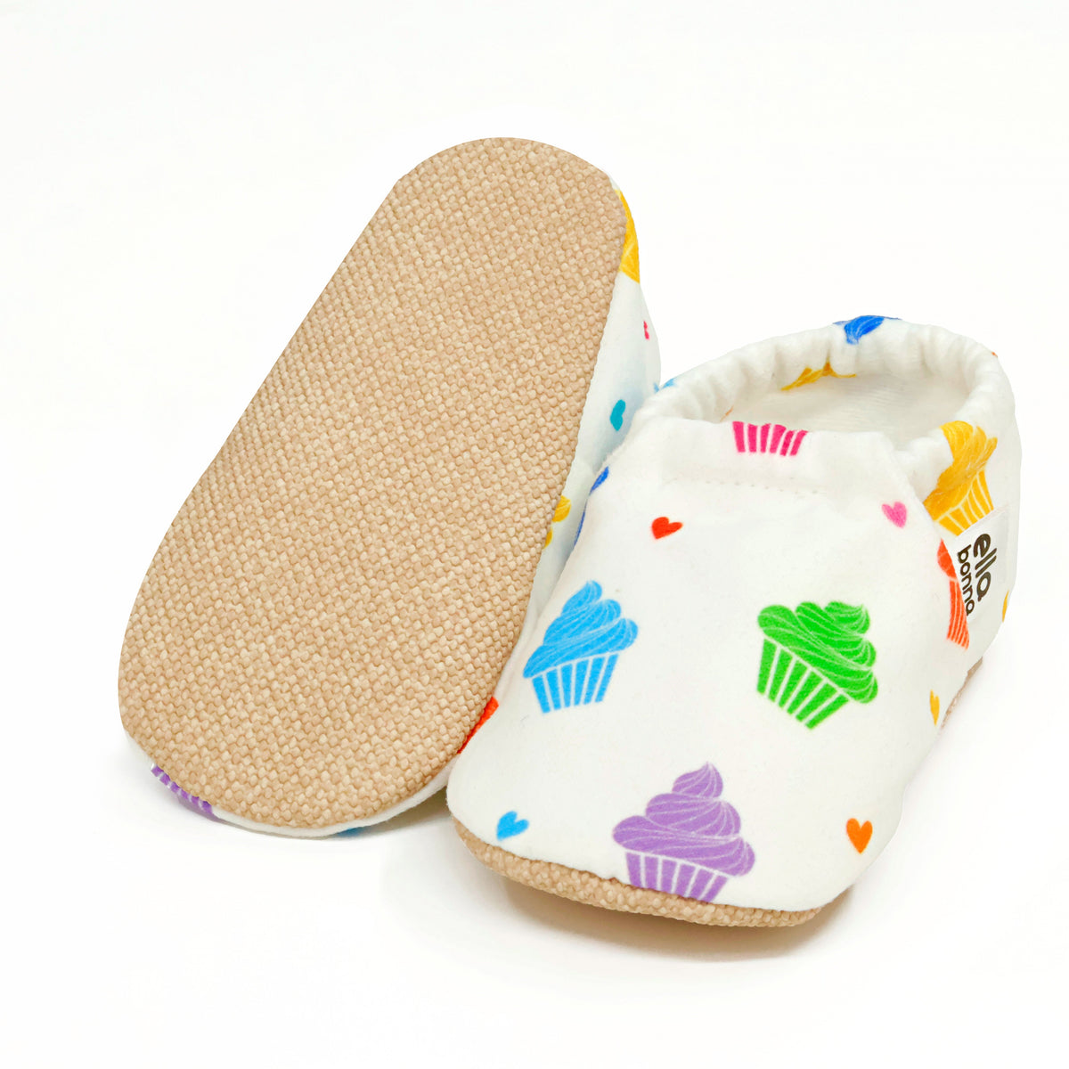 White slip-on baby moccasins with colorful cupcake print, with one sole facing the camera on a white background.