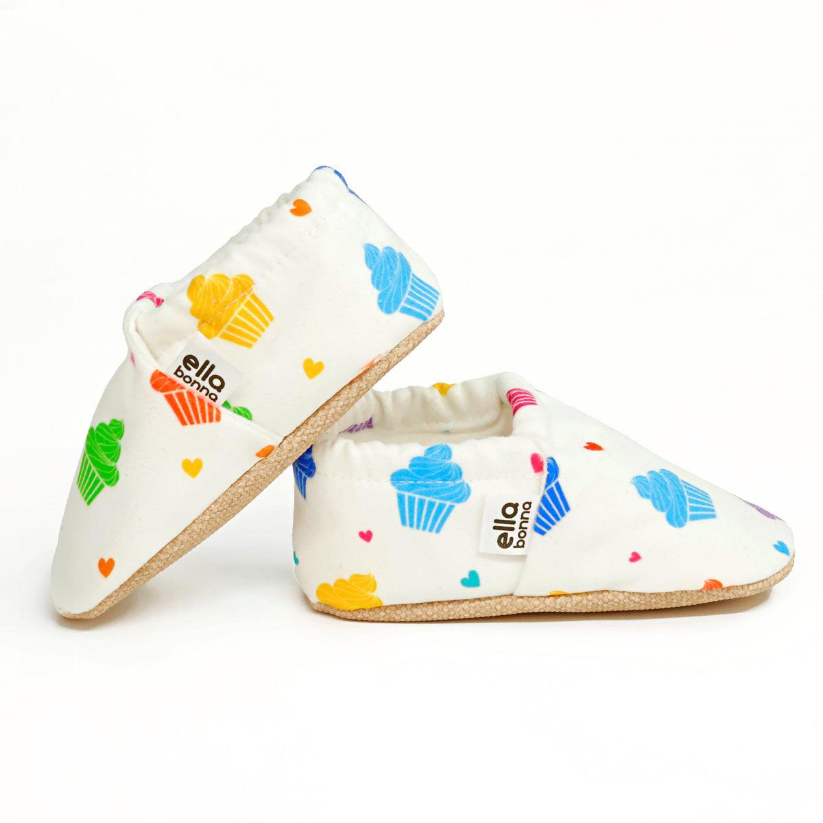 Side views of white slip-on baby moccasins with colorful cupcake print on a white background.