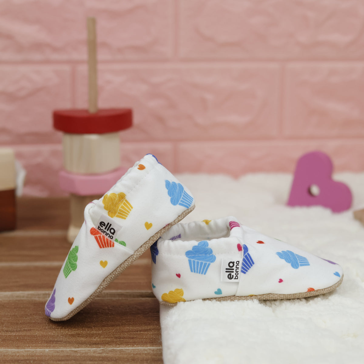 White slip-on baby moccasins with colorful cupcake print arranged together to show the sides and uppers.