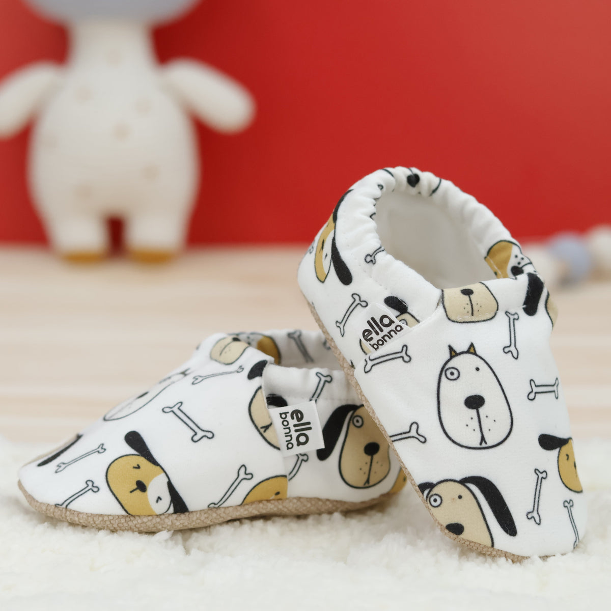 Cream slip-on baby moccasins with dog faces and bone print arranged together to show the sides and uppers.