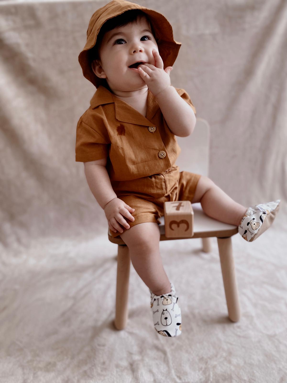 Child seated on a stool in a brown outfit wearing dog-print moccasins.