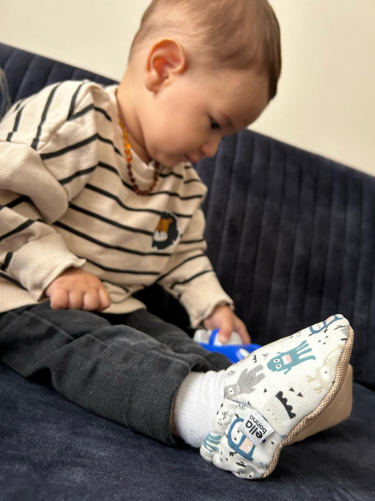 Child seated on a sofa looking at monster-print moccasins.