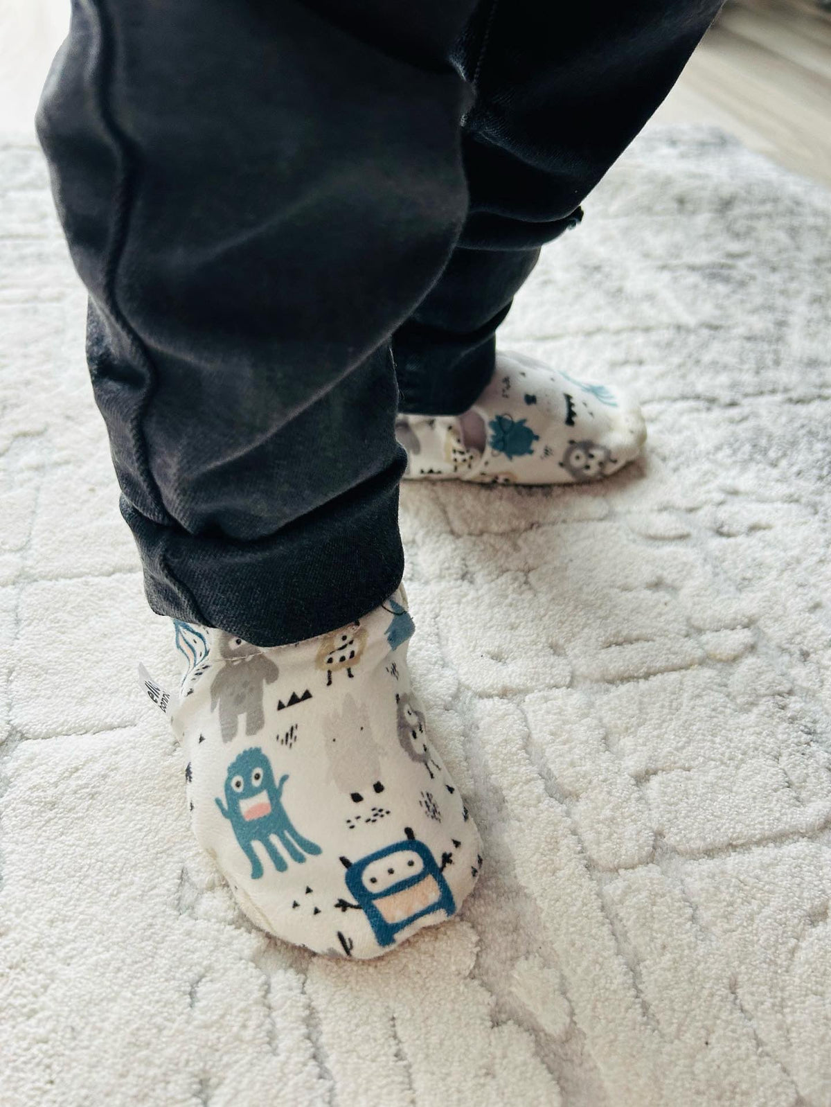 Close-up of monster-print moccasins worn while standing on a rug.