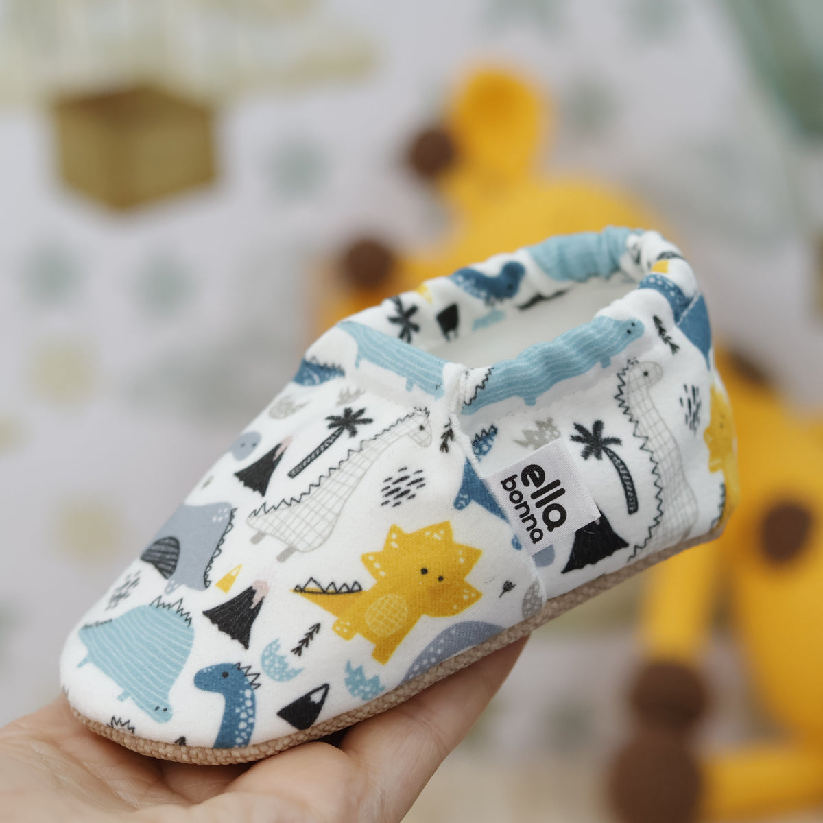 Single dinosaur-print moccasin held in a hand.