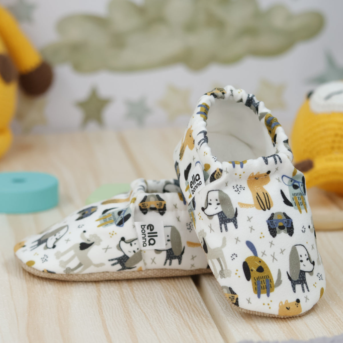 Cream slip-on baby moccasins with yellow, blue and gray dog print arranged together to show the sides and uppers.