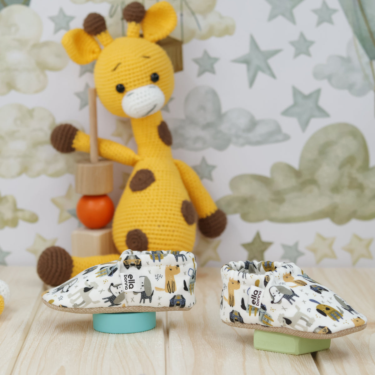 Cream slip-on baby moccasins with yellow, blue and gray dog print arranged side by side on a tabletop.