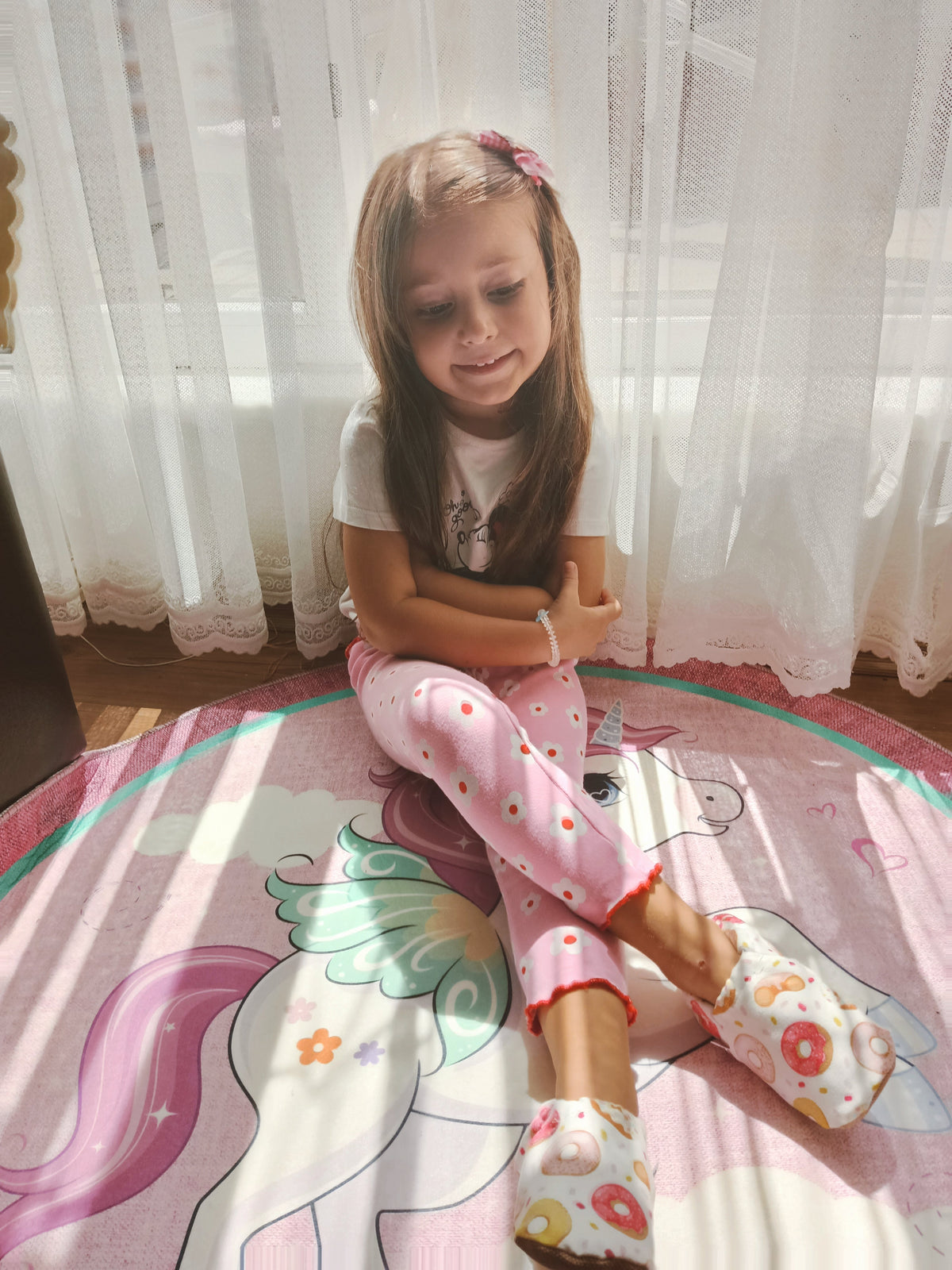 Child seated by a window wearing doughnut-print moccasins.