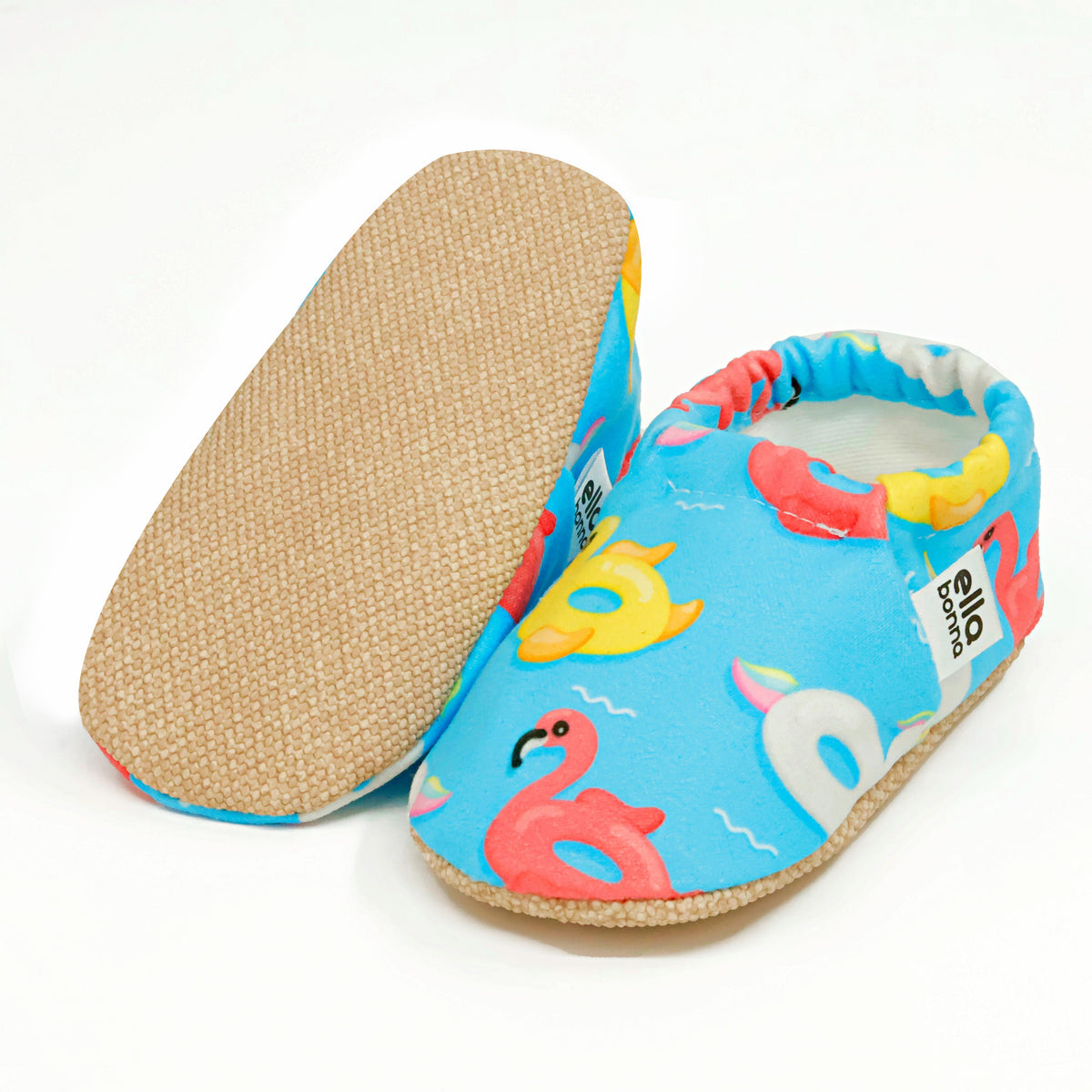 Blue slip-on baby moccasins with colorful duck, swan and flamingo pool-float print, with one sole facing the camera on a white background.