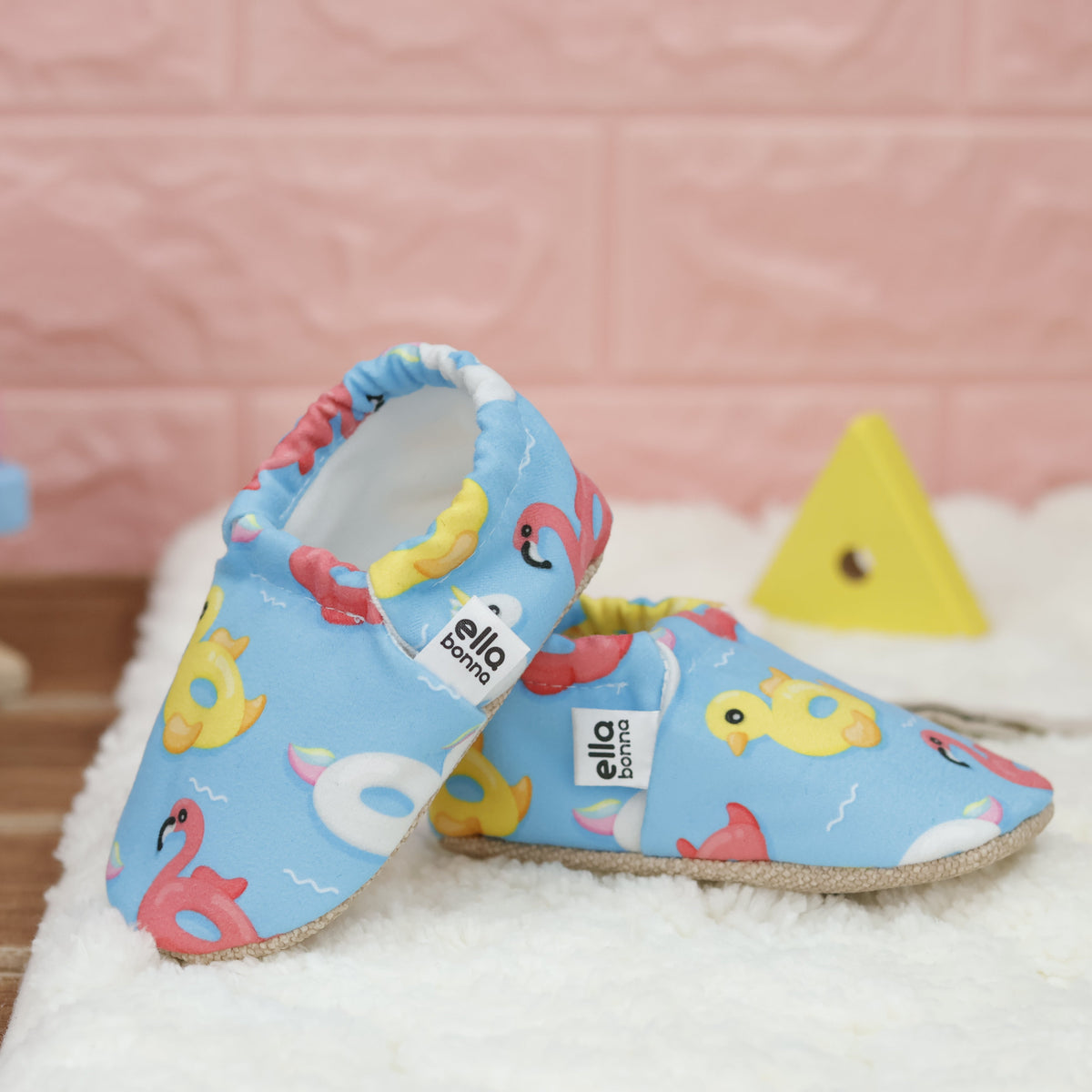 Blue slip-on baby moccasins with colorful duck, swan and flamingo pool-float print arranged together to show the sides and uppers.
