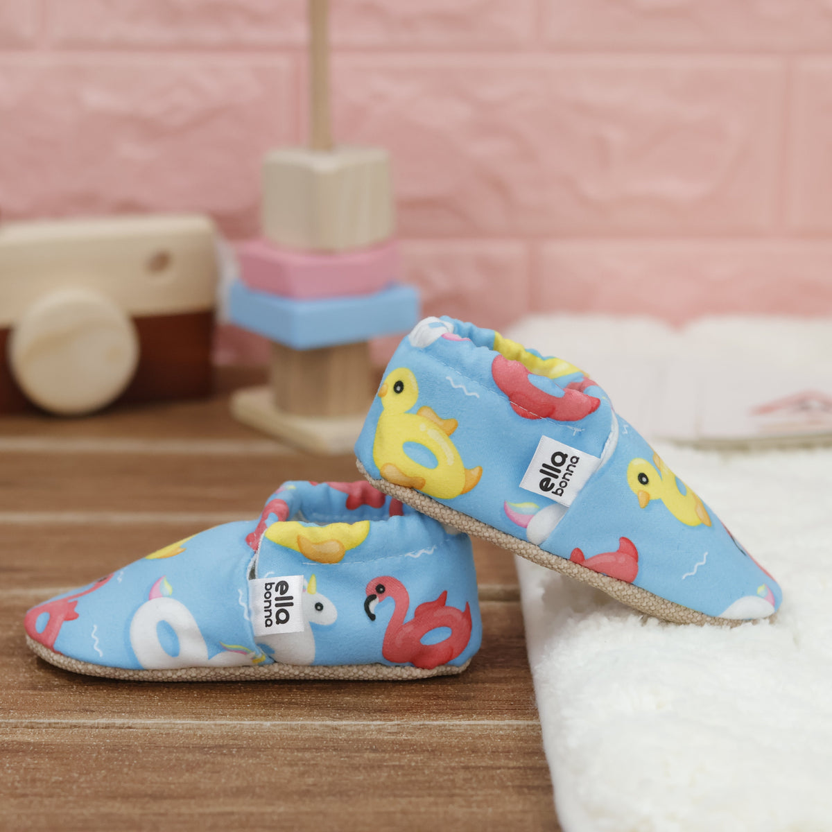 Blue slip-on baby moccasins with colorful duck, swan and flamingo pool-float print arranged together to show the sides and uppers.