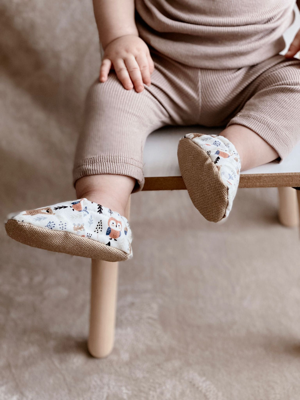 Close-up of woodland-print moccasins worn by a child seated on a stool.