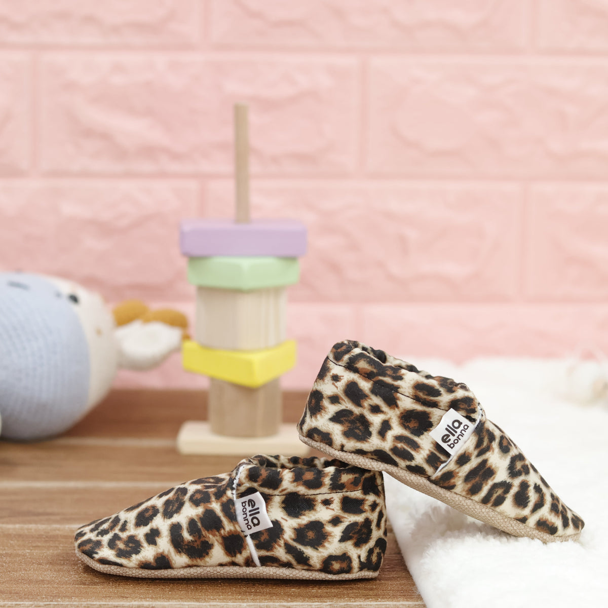 Tan slip-on baby moccasins with brown-and-black leopard spots arranged together to show the sides and uppers.