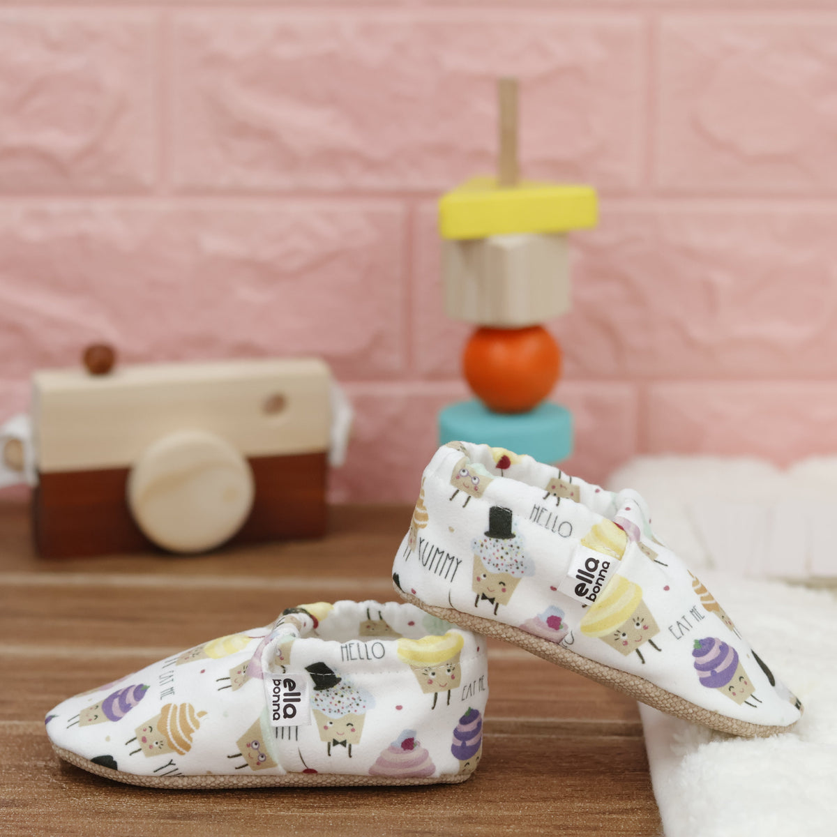 Cream slip-on baby moccasins with pastel cupcake print arranged together to show the sides and uppers.