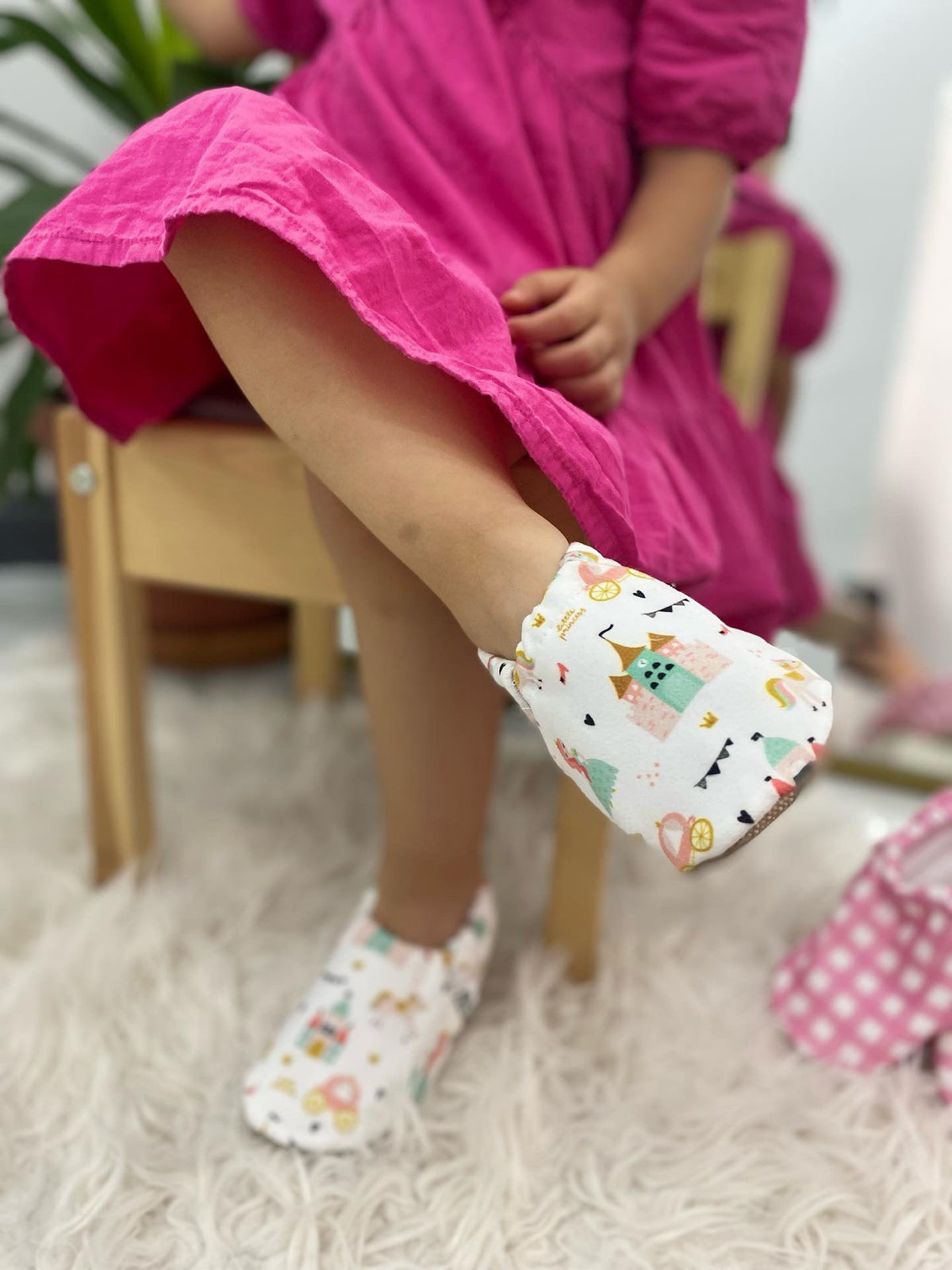 Side close-up of princess-print moccasins worn by a seated child.
