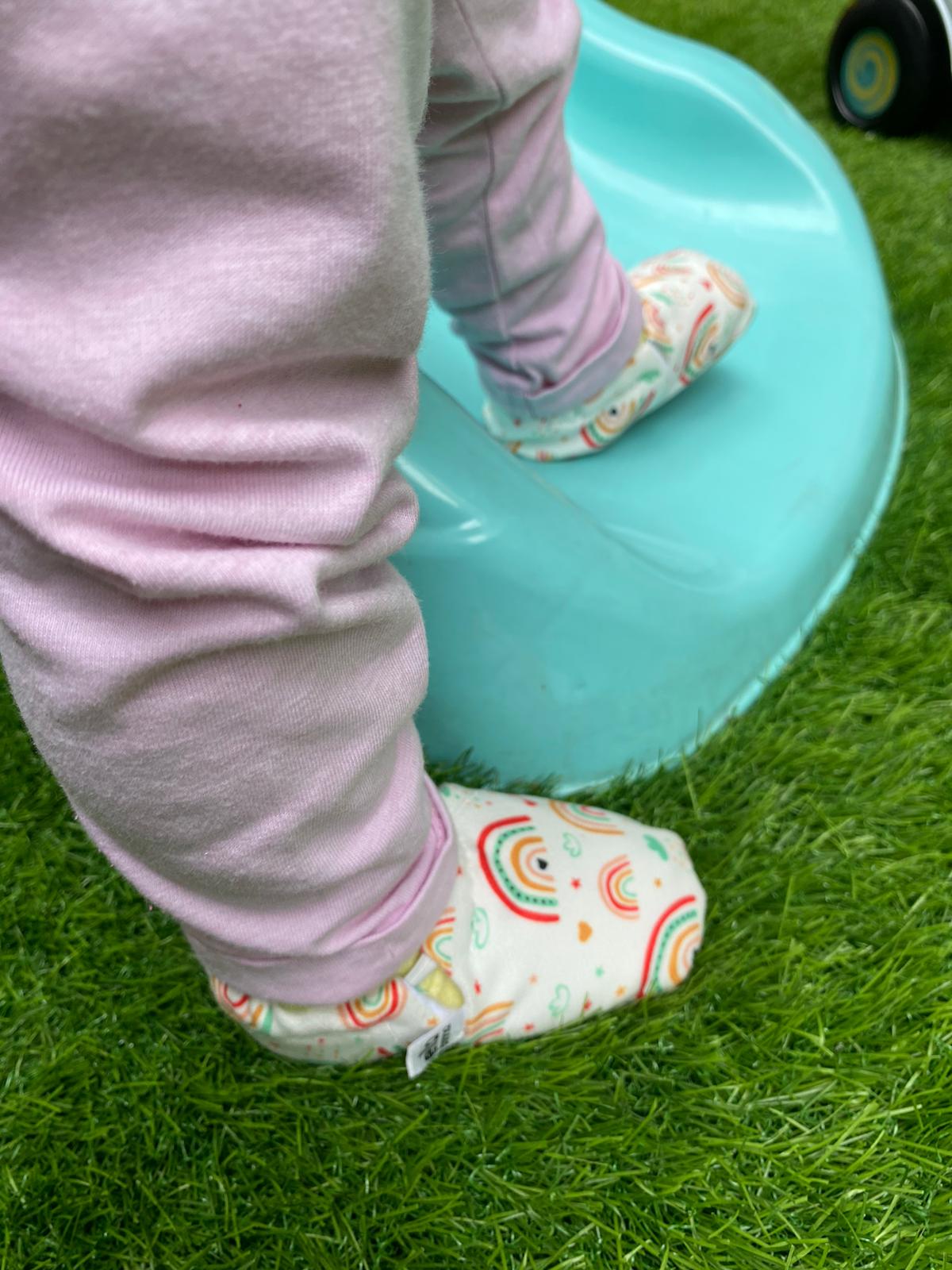 Rainbow-print moccasins worn with purple trousers beside a slide.