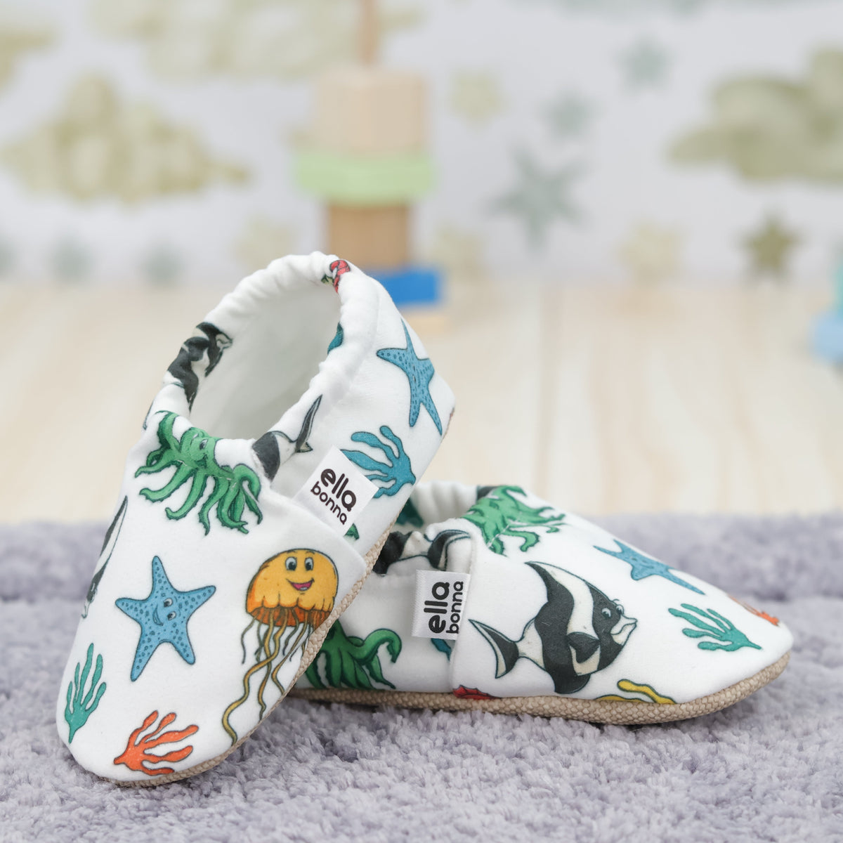 Cream slip-on baby moccasins with colorful sea animals and starfish arranged together to show the sides and uppers.