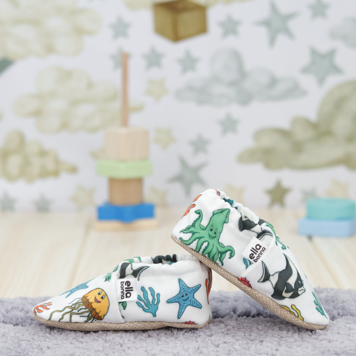 Cream slip-on baby moccasins with colorful sea animals and starfish arranged together to show the sides and uppers.