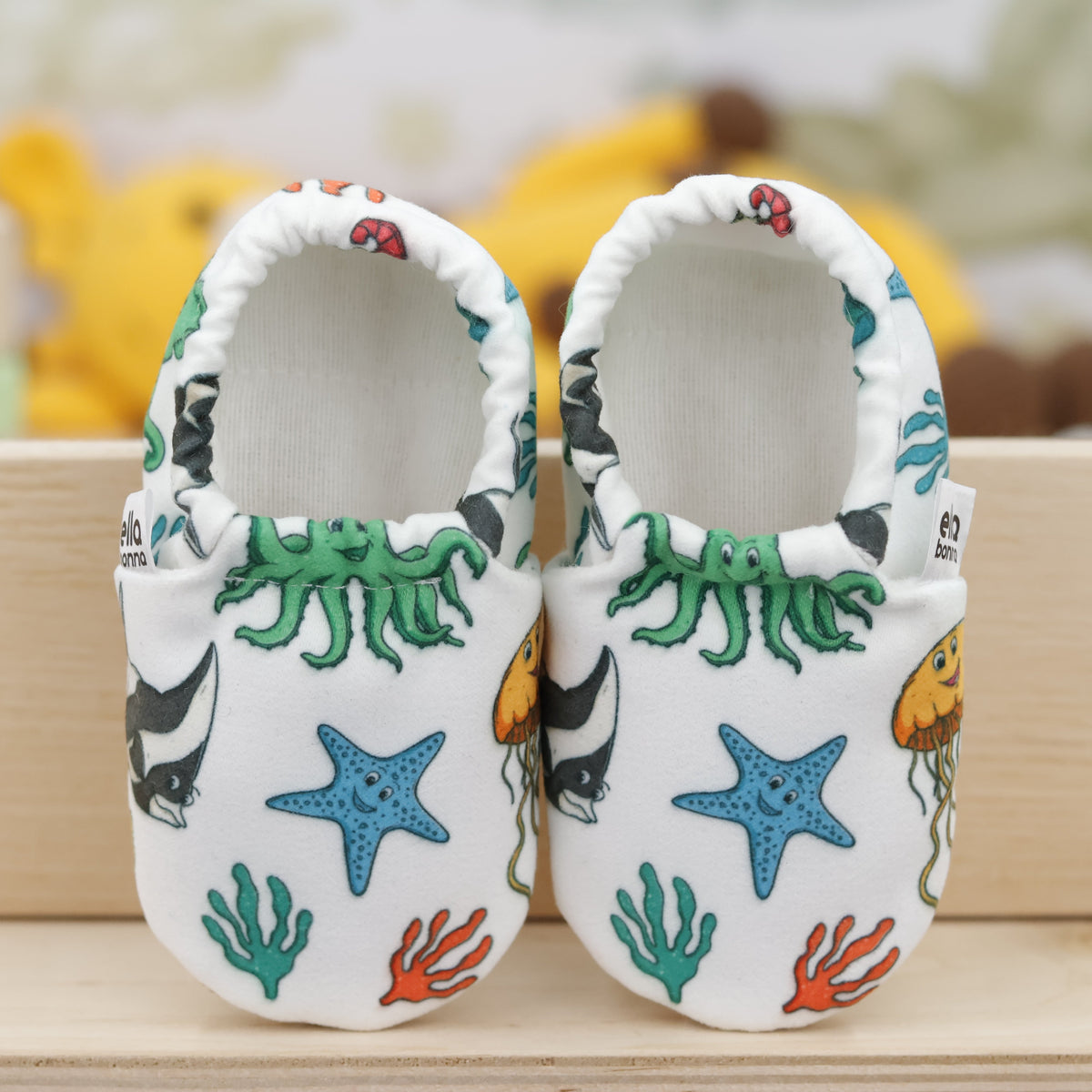 Pair of cream slip-on baby moccasins with colorful sea animals and starfish, showing the openings and uppers.