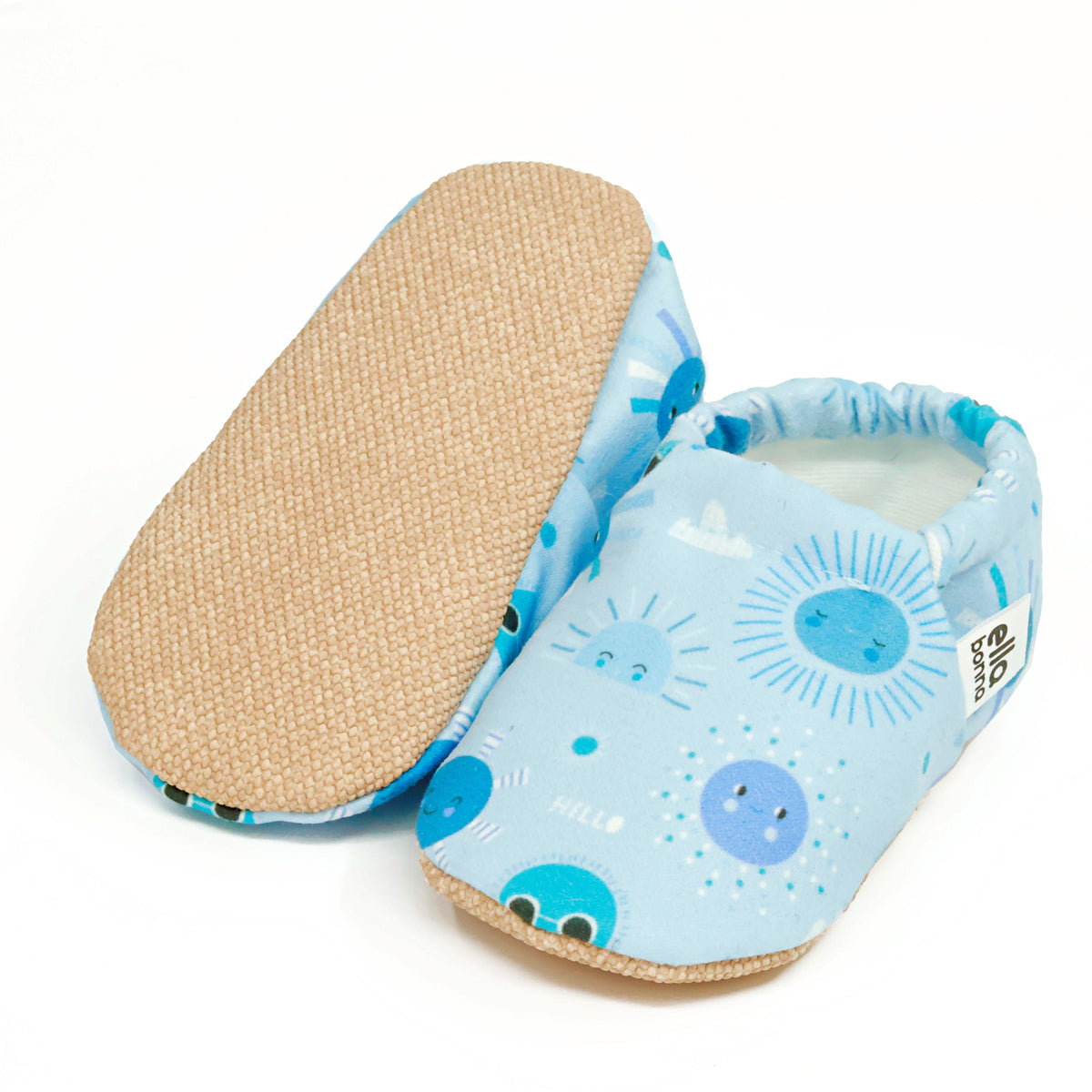 Light blue slip-on baby moccasins with blue sun and moon print, with one sole facing the camera on a white background.