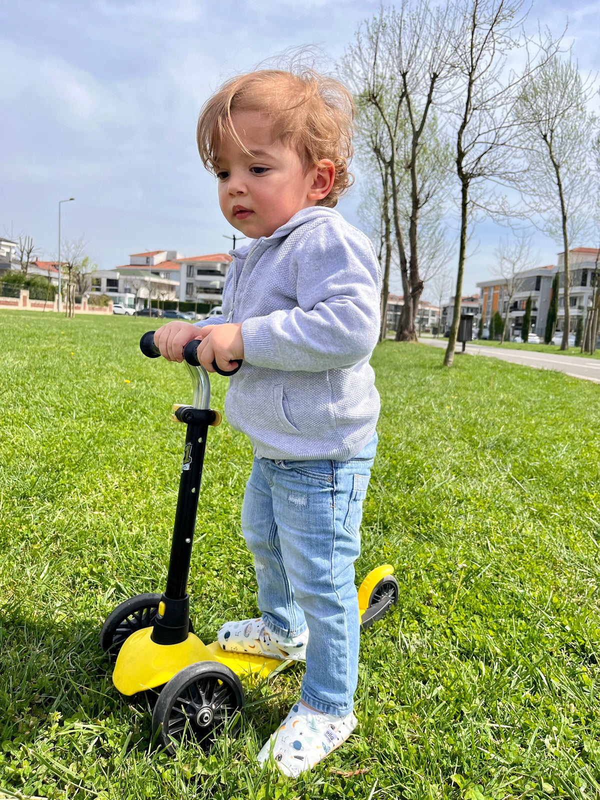 Child standing on grass with a scooter wearing space-print moccasins.