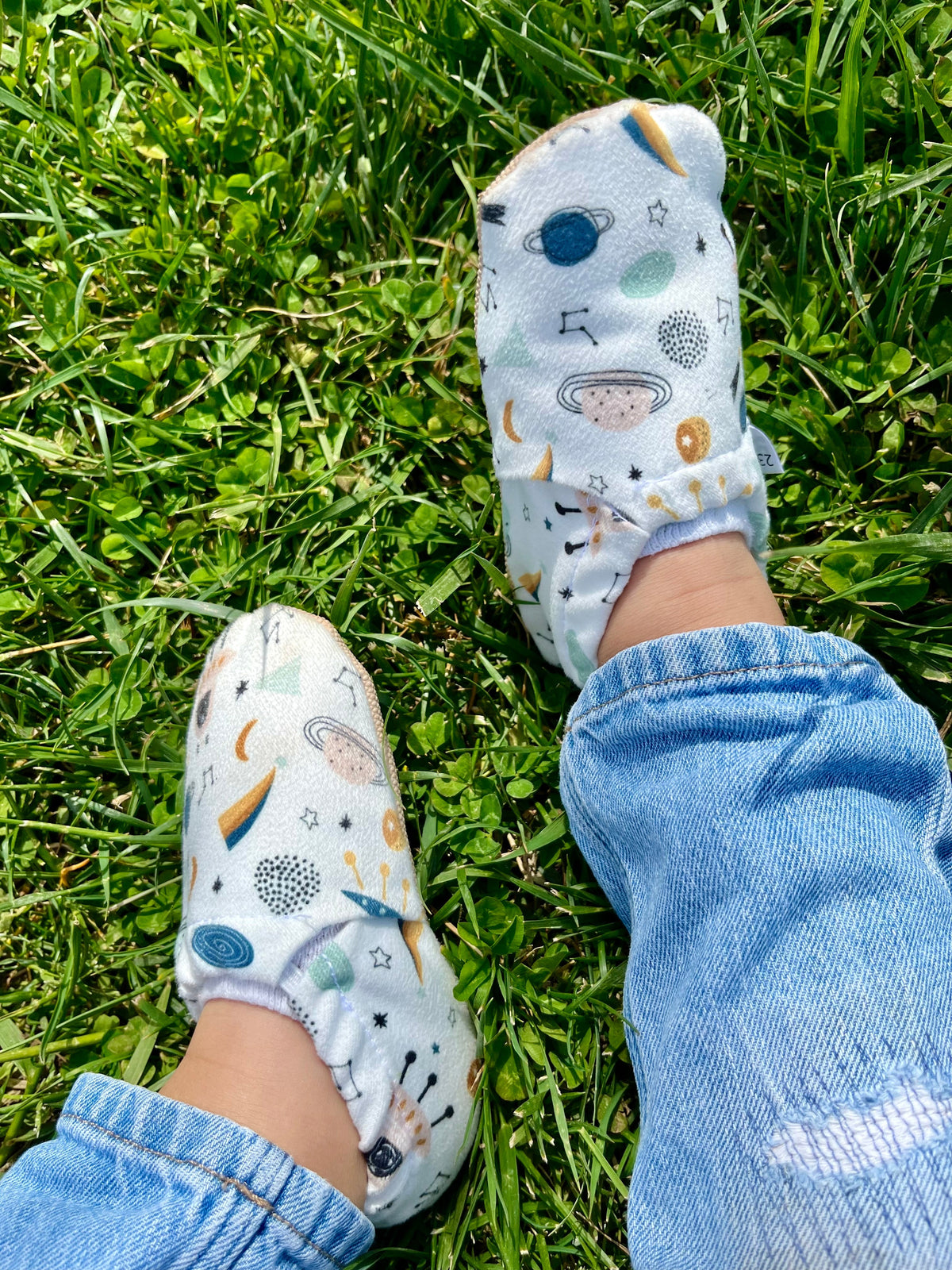 Close-up of space-print moccasins worn with jeans on grass.
