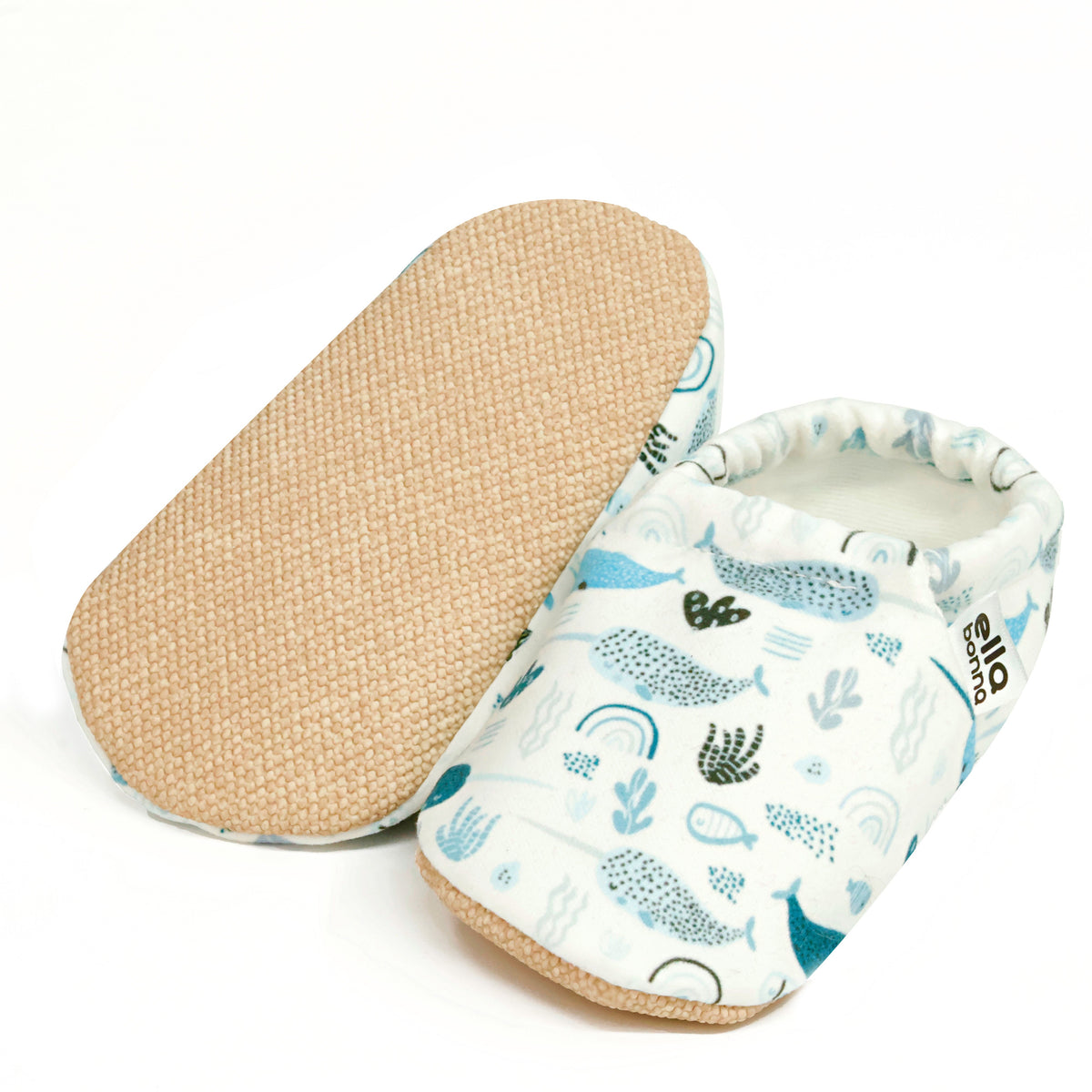 Cream slip-on baby moccasins with blue sea-creature print, with one sole facing the camera on a white background.
