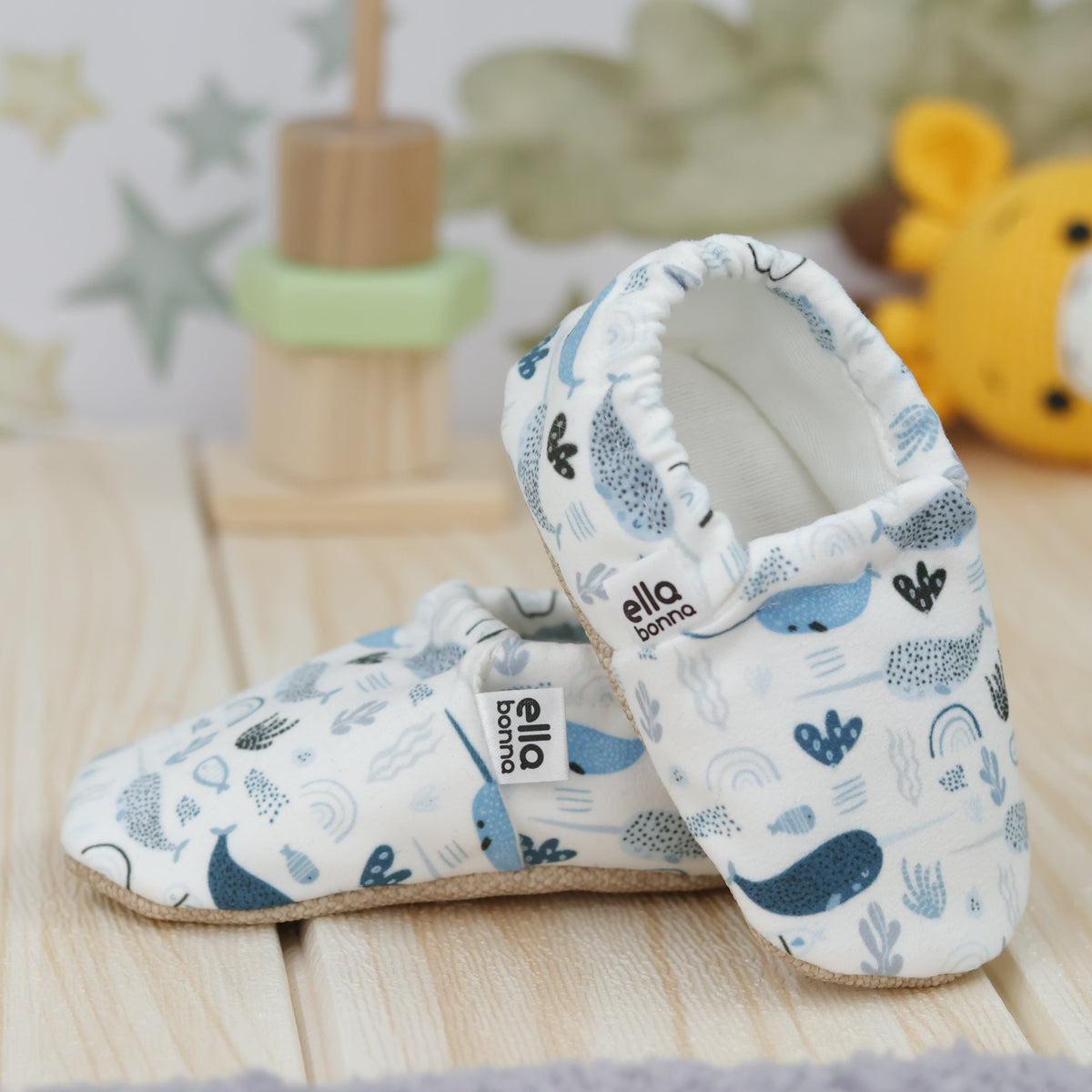 Cream slip-on baby moccasins with blue sea-creature print arranged together to show the sides and uppers.
