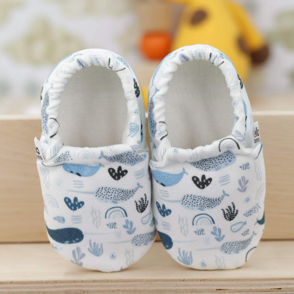 Pair of cream slip-on baby moccasins with blue sea-creature print, showing the openings and uppers.