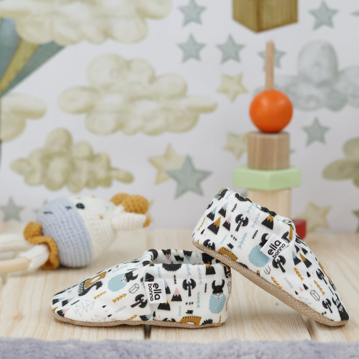 Cream slip-on baby moccasins with Viking ship and mountain print arranged together to show the sides and uppers.