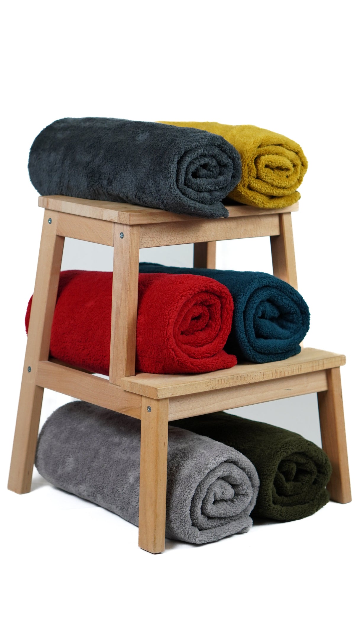 Rolled fleece blankets in assorted colors arranged on a wooden stool.