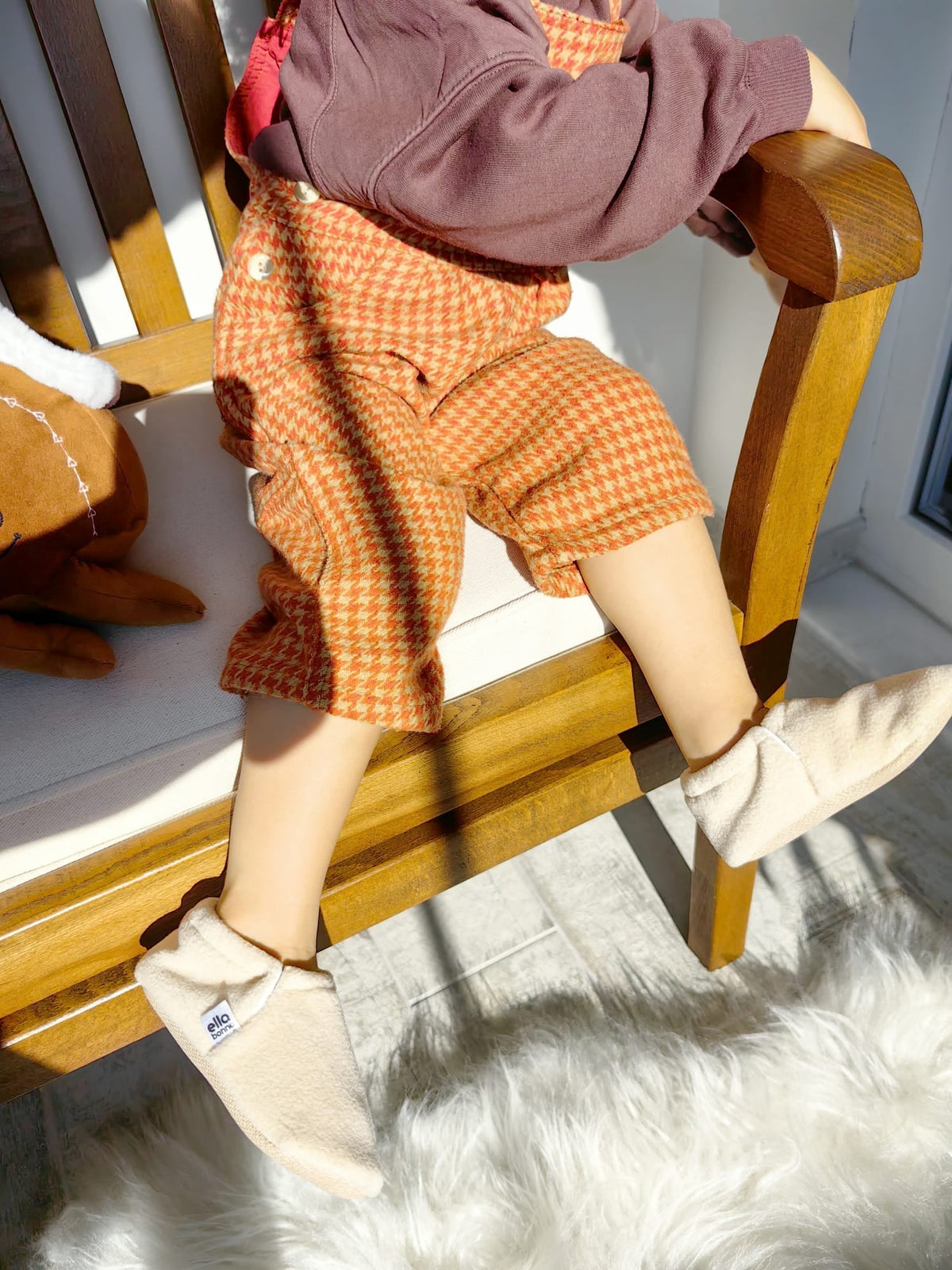 Close-up of cream fleece moccasins worn by a child seated on a chair.